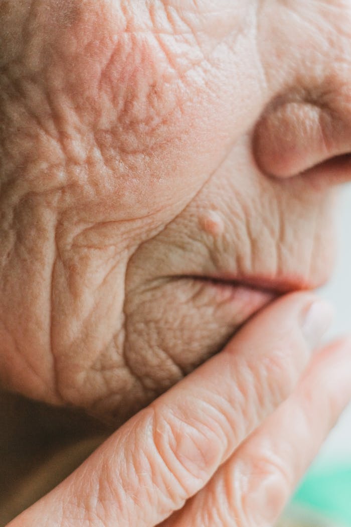 gallery-1 Detailed close-up of a senior adult's face and hand, highlighting wrinkles and aged skin.
